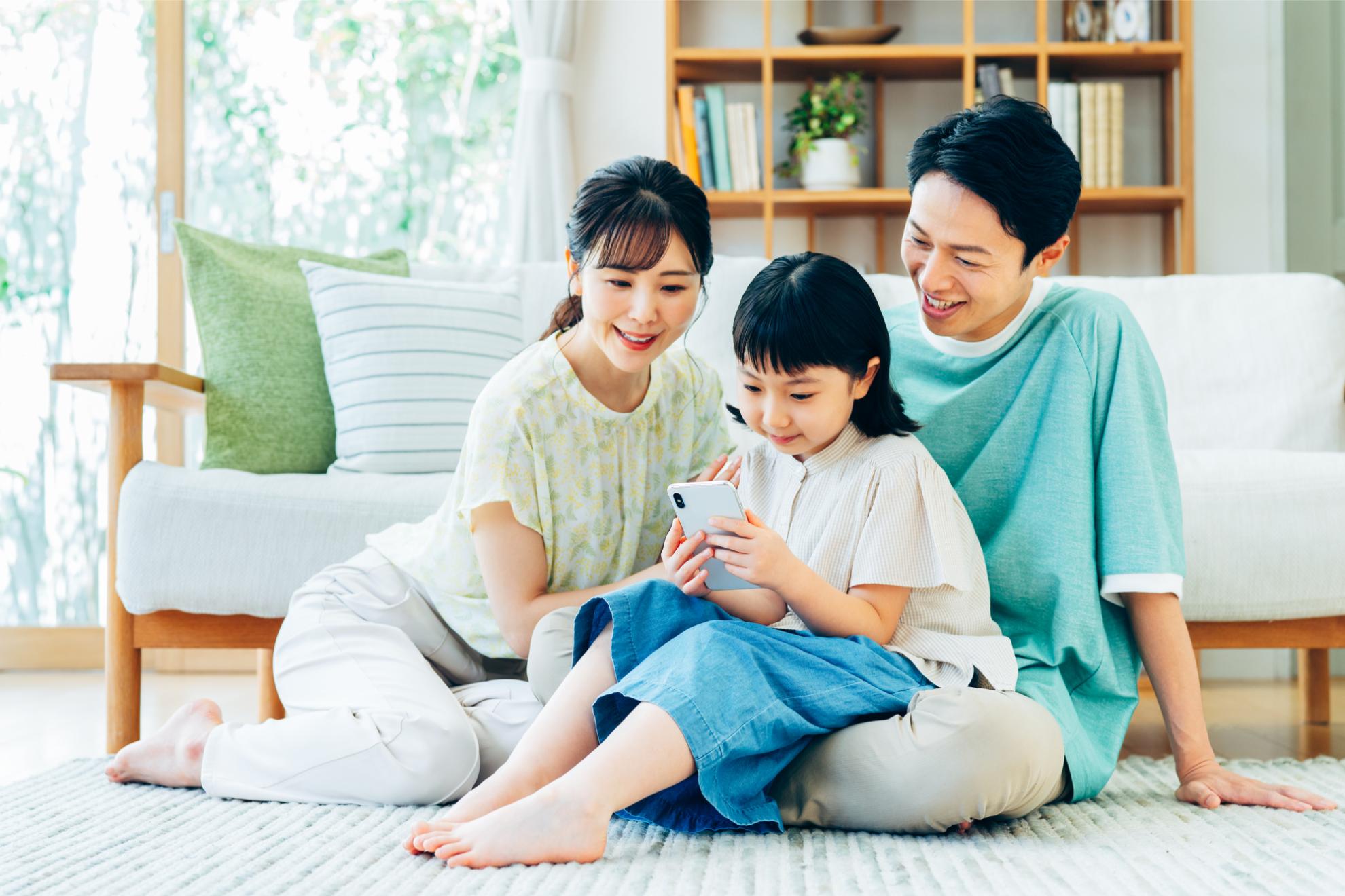 スマートフォンを見ながら笑顔で過ごす3人家族