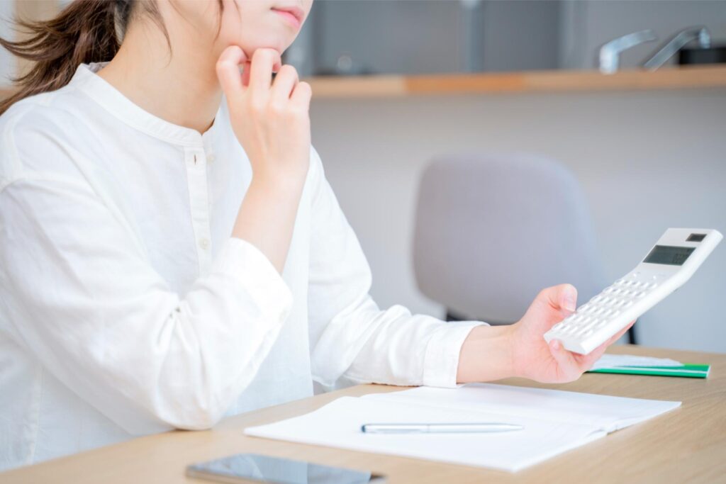 電卓を持ち家計簿について考え込む女性
