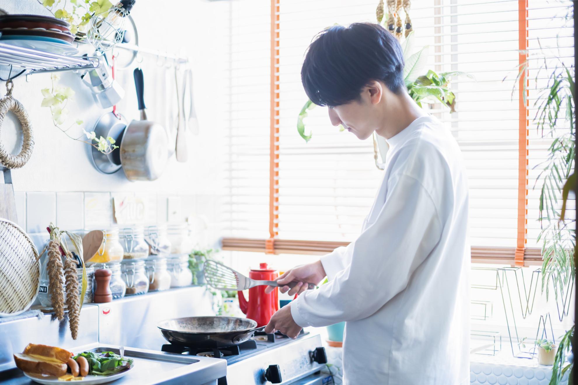 明るいキッチンでガスコンロを使って調理をする男性