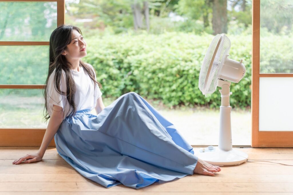 縁側で扇風機にあたって涼む女性