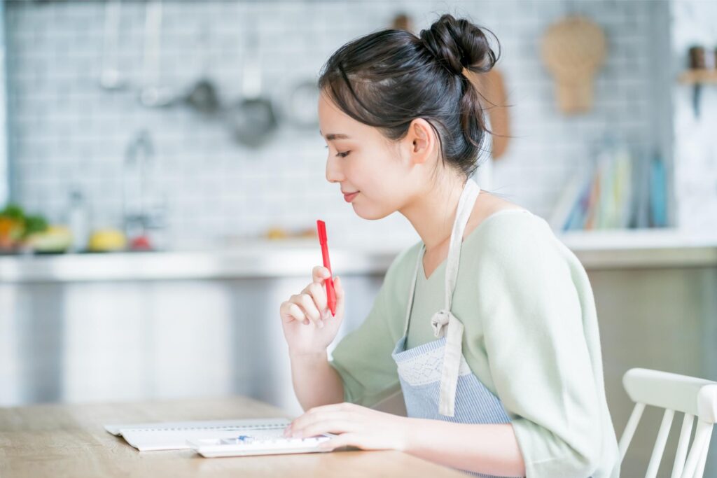 キッチンで電卓を使い、家計簿や光熱費の計算をする女性